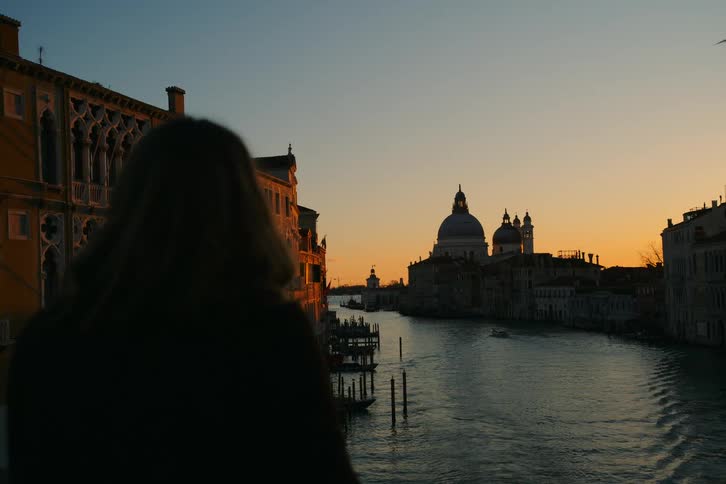 Silhouette of a woman looking out over the Grand Canal in Venice, Italy during a beautiful golden hour sunset