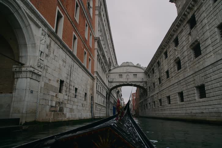 A point-of-view from a gondola as it emerges from under a bridge to reveal the iconic Bridge of Sighs in a Venetian canal