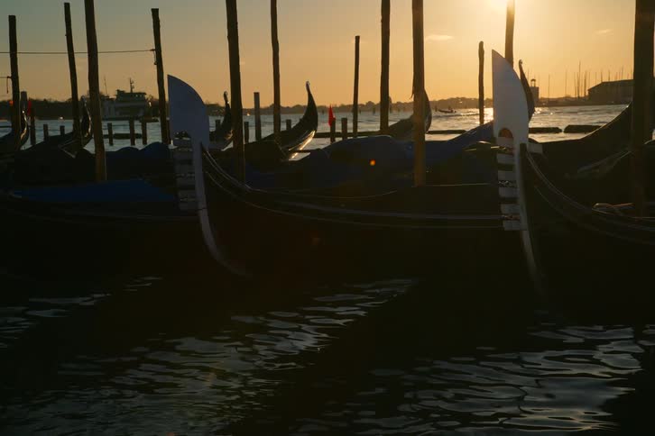 Traditional gondolas moored on the Venetian lagoon are silhouetted against a beautiful golden sunset
