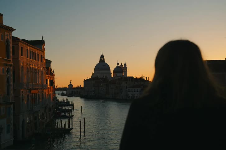 A woman in silhouette watches the sunset over the Grand Canal and the Basilica di Santa Maria della Salute in Venice, Italy