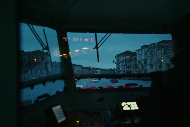 From the dimly lit cabin of a water bus, the iconic Grand Canal of Venice unfolds under a moody twilight sky