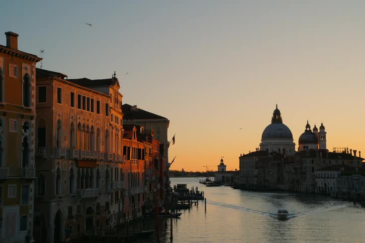 Golden hour light illuminates the historic architecture along the Grand Canal in Venice, Italy, as a water taxi sails past