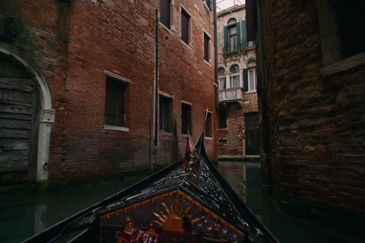 A first-person perspective from a gondola as it glides slowly through a narrow, historic canal in Venice, Italy