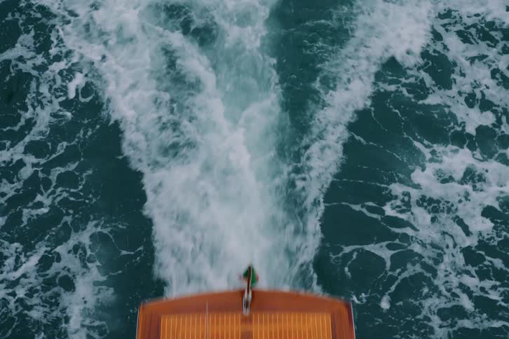 A luxurious wooden motorboat cruises through deep blue water, shot from directly above