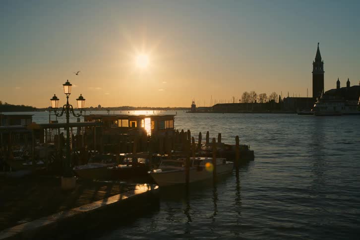 A serene sunset over the Venice lagoon, silhouetting the island of San Giorgio Maggiore and boats moored at a dock