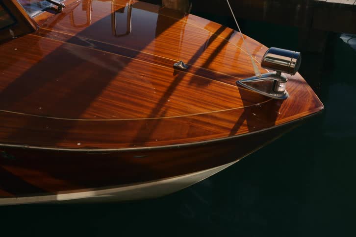 Sunlight glistens on the polished mahogany deck of a classic wooden boat moored in a tranquil marina