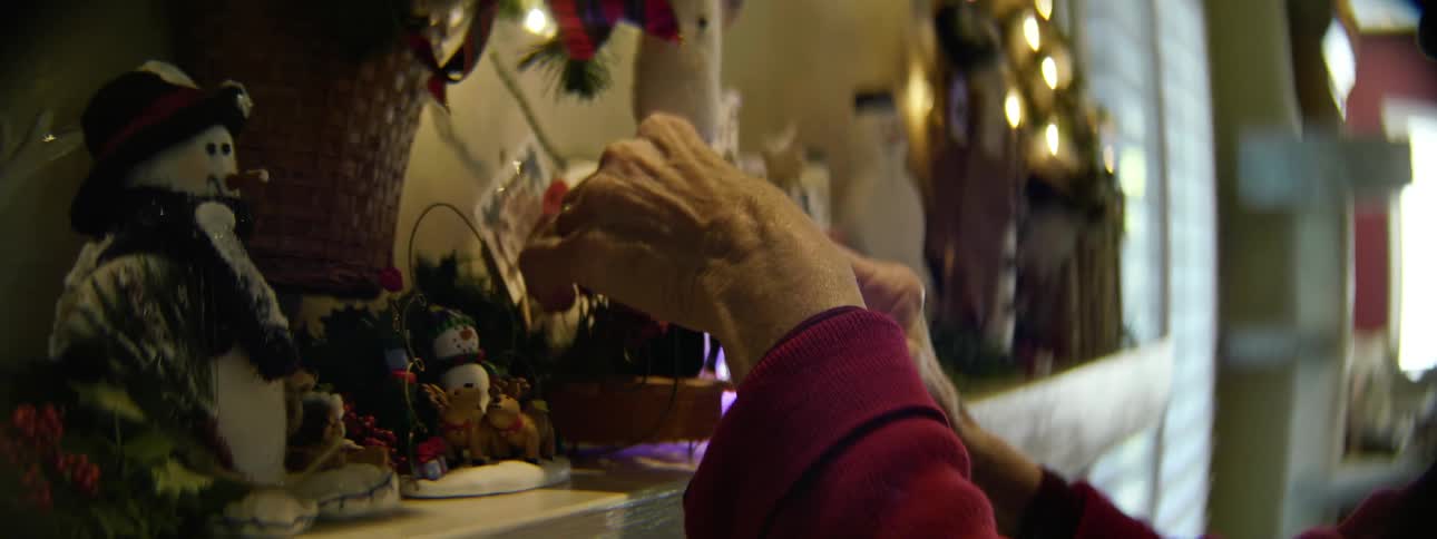 An older woman arranges christmas decorations on a mantle