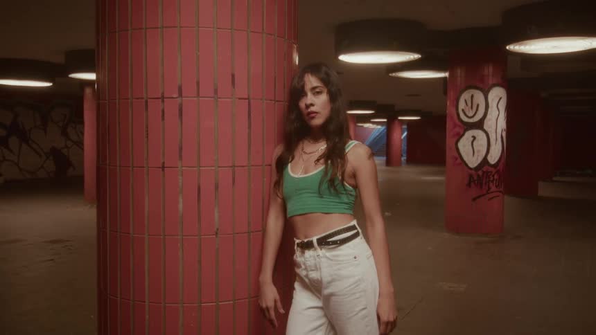A confident young woman with an edgy style looks at the camera while posing in a moody, urban underground space