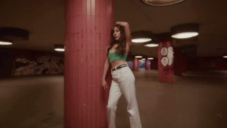 A confident young woman on roller skates poses against a red pillar in a gritty, graffiti-covered underpass