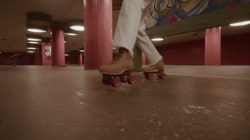 A woman joyfully dances on rollerskates in a gritty, graffiti-covered underground tunnel