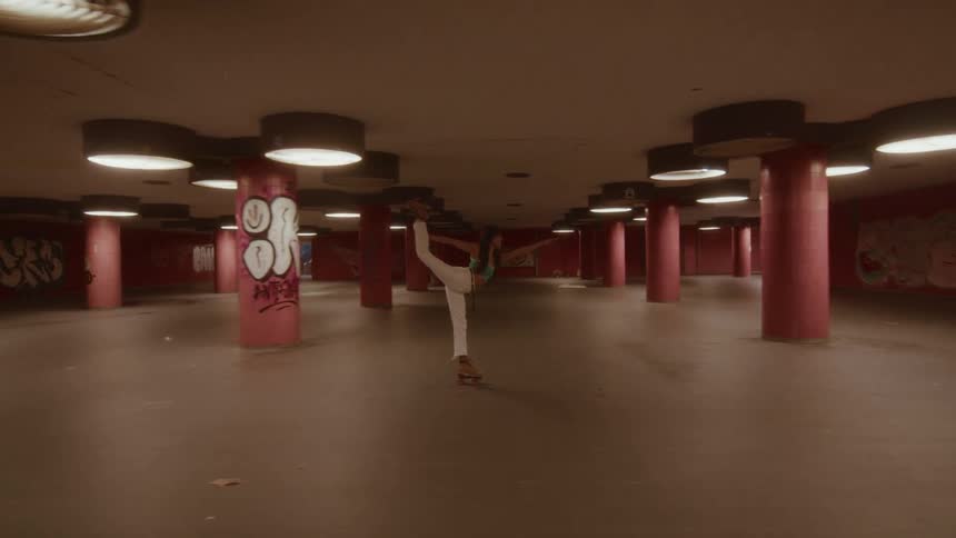 A woman gracefully holds a standing split on roller skates while gliding through a graffiti-covered underground space