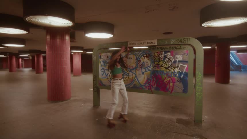 A stylish woman joyfully dances on her roller skates in a gritty, graffiti-covered urban underpass