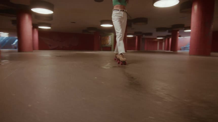 Low-angle tracking shot of a woman in white jeans roller skating backward through a gritty, graffiti-covered underground passage