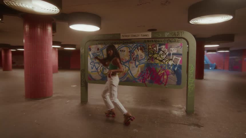 A stylish young woman grooves on her roller skates as she dances alone in a deserted, graffiti-covered urban underpass