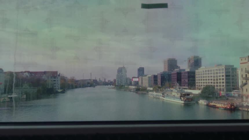 A nostalgic view of the Berlin cityscape and the Spree River, as seen from the window of a moving train crossing a bridge