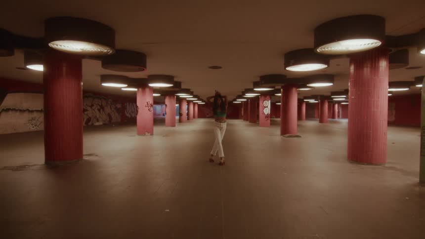 A woman playfully roller skates and dances away from the camera in a graffiti-covered underground tunnel
