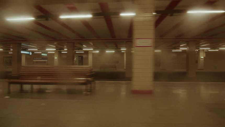 POV from a train window looking out at an empty, fluorescent-lit subway station as the train departs and enters a dark tunnel