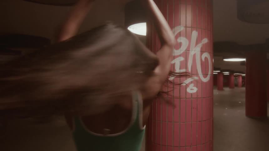A stylish young woman joyfully whips her long hair back and forth while dancing in a gritty urban underpass