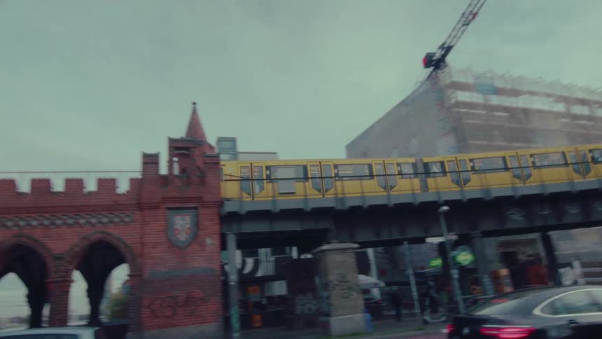 A slow-motion tracking shot follows a yellow train as it crosses the iconic Oberbaum Bridge in Berlin, Germany, with city traffic below