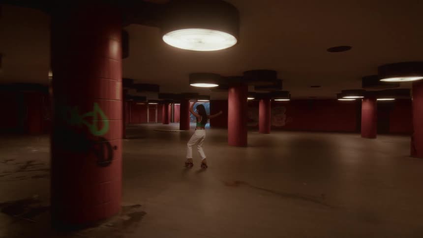 A stylish woman gracefully dances on roller skates as she glides through a dimly lit urban underpass in slow motion
