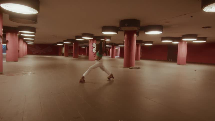 A long-haired woman gracefully roller skates through an empty, graffiti-tagged urban underpass