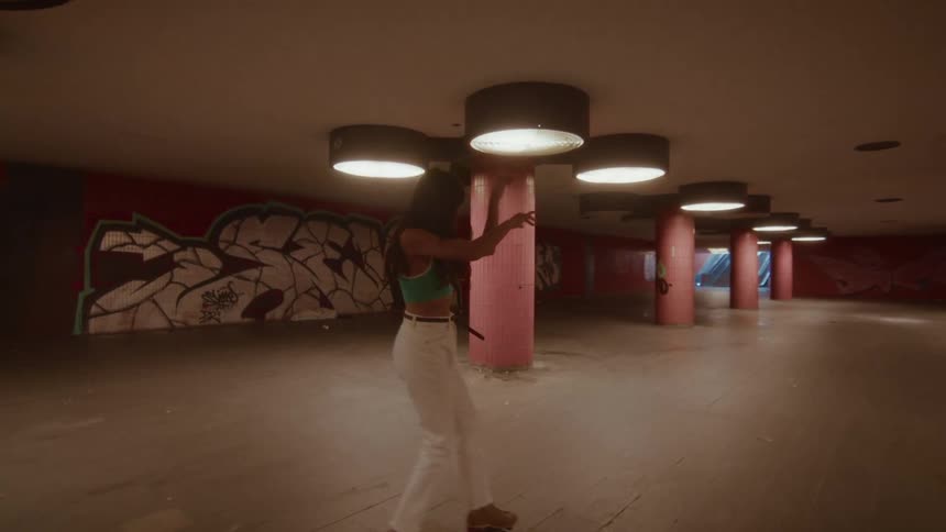 A stylish woman joyfully dances on roller skates through a dimly lit, graffiti-covered underground passage