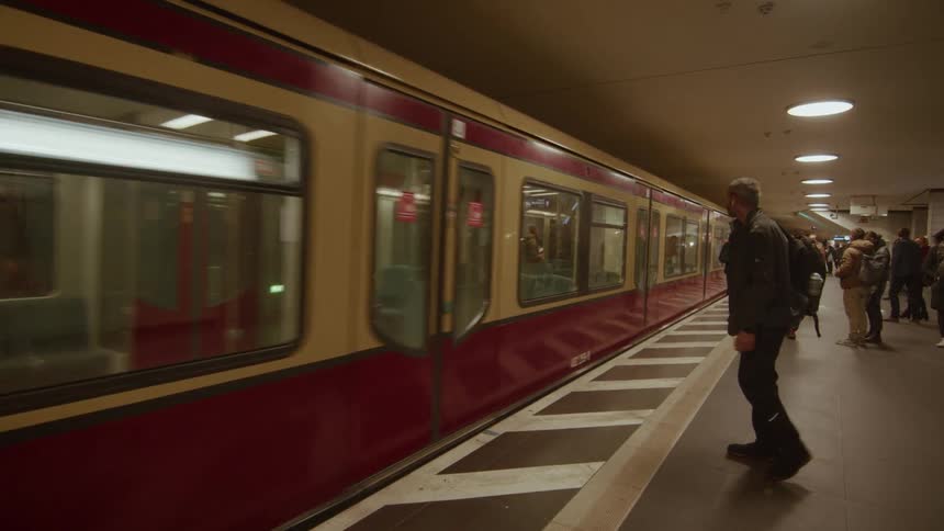 A man waits on an underground platform as a subway train slowly pulls into the station
