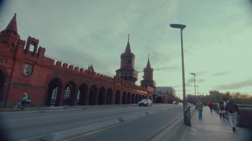 A cinematic wide-angle view of the historic Oberbaum Bridge in Berlin with traffic and pedestrians during a cloudy sunset