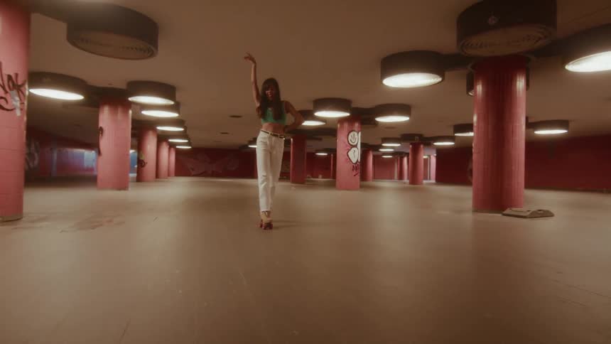 A stylish woman joyfully dances on roller skates through a retro-style underground passage with pink pillars