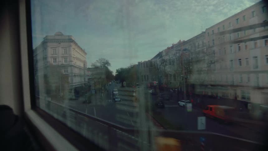 An atmospheric point-of-view shot from an elevated train window, capturing the moody cityscape passing by at dusk with reflections on the glass