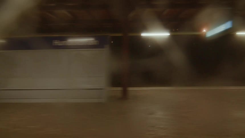 A blurry point-of-view from a moving train window at night passing through a graffiti-covered subway station