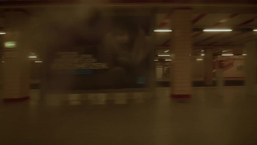 A dreamy, blurry point-of-view shot from a moving subway train as it passes through a dimly lit underground station