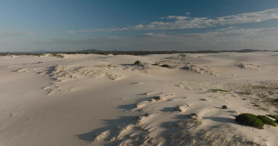 A slow aerial flight over vast, rolling white sand dunes under a clear blue sky at sunrise