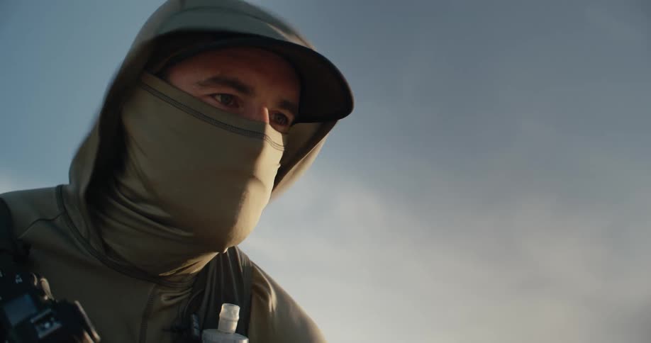 A mysterious man wearing a hood and face covering looks up with determination in slow motion