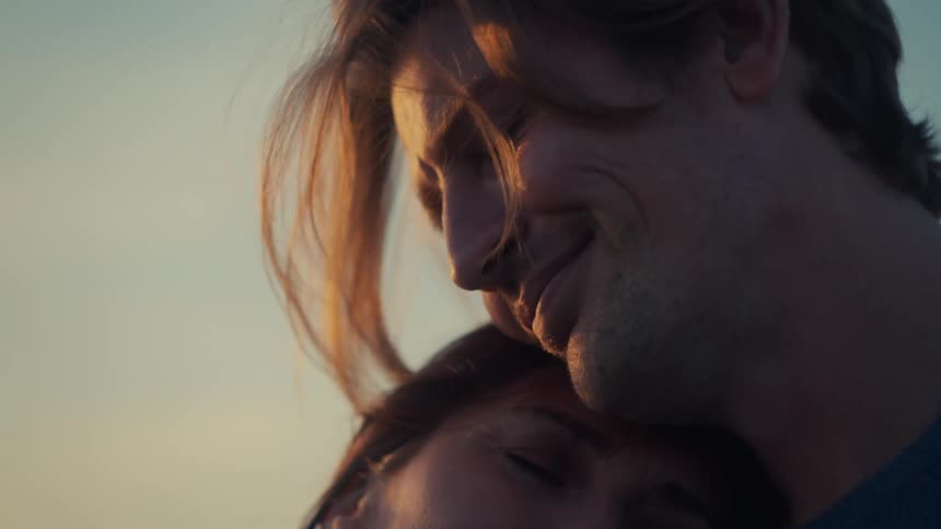 A romantic couple embraces tenderly, their faces illuminated by the warm glow of the setting sun