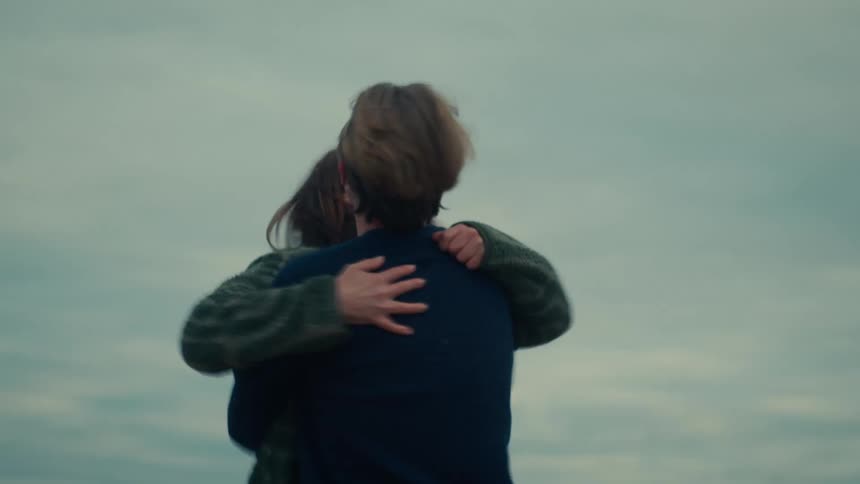 A woman runs into her boyfriend's arms as he joyfully picks her up and spins her around in a slow-motion, loving embrace on a windy day