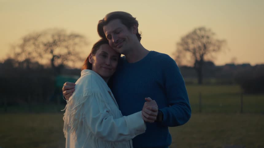 A romantic couple shares an intimate moment while slow dancing together in a countryside field during a beautiful golden hour