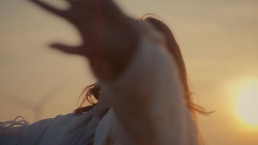 Backlit by the golden sunset, a woman in a white fringed jacket turns and lifts her arms in a slow, graceful motion of freedom