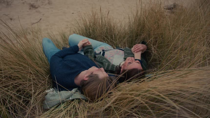 From a high angle, a romantic couple relaxes together in the tall beach grass on a sand dune