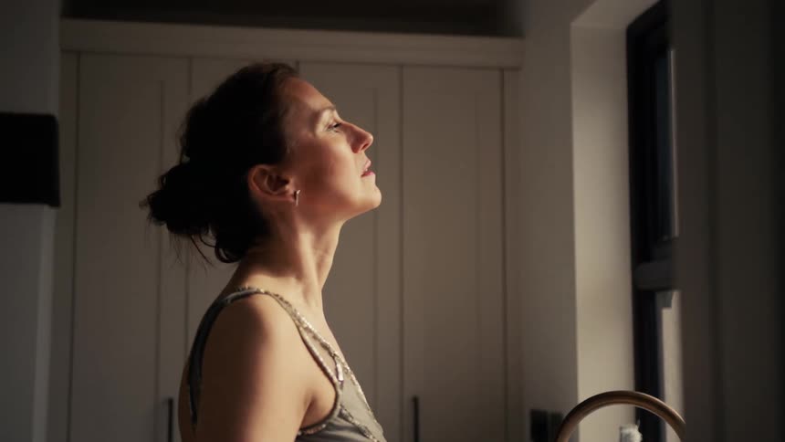 A serene woman in a glamorous dress enjoys a moment of peaceful contemplation in her sunlit kitchen