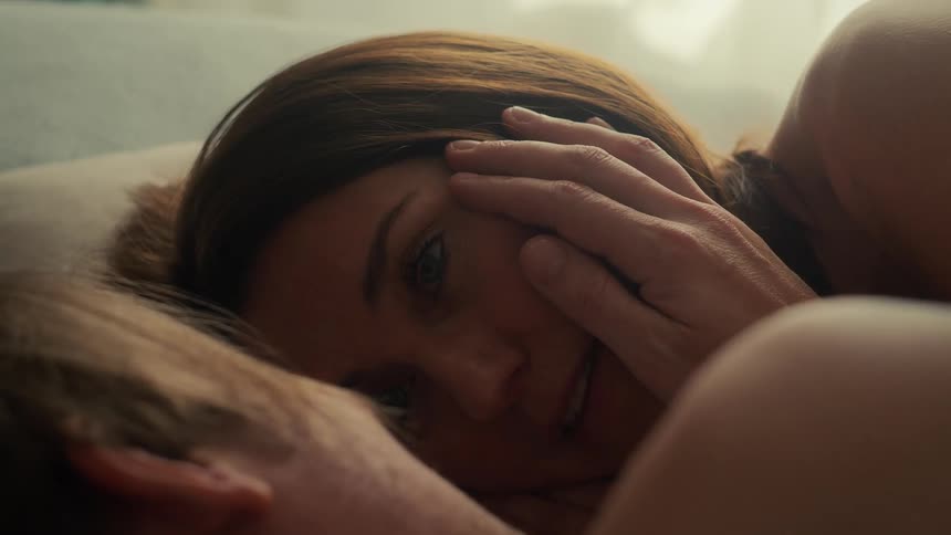 A loving couple shares a tender, intimate moment in bed as the man gently caresses the woman's face