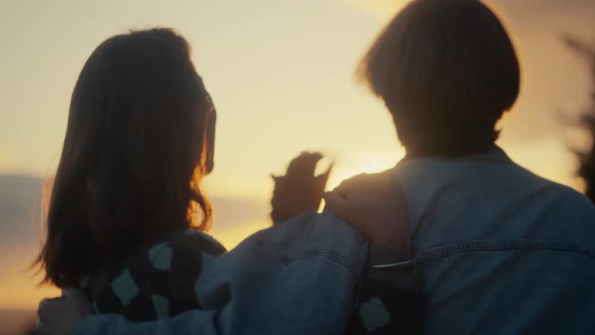 A happy young couple laughs and embraces in slow motion, silhouetted by the warm glow of the setting sun