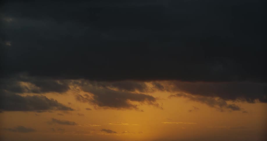 Dark storm clouds gather over the horizon as the golden light of sunset glows below