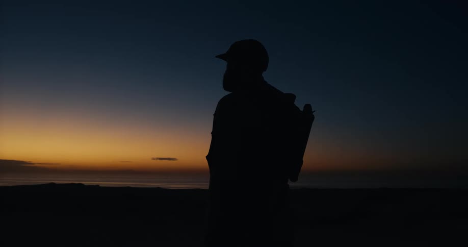A lone adventurer in silhouette walks into the frame to observe the tranquil sunrise over the ocean