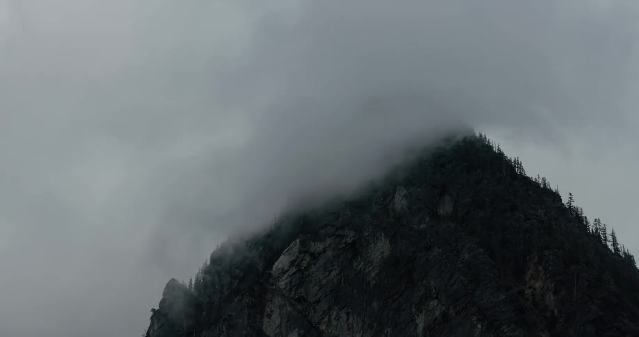 Foggy clouds move slowly across a dramatic, dark mountain peak