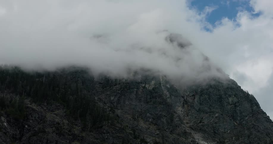 A dramatic time-lapse reveals a rugged mountain peak as a thick blanket of clouds slowly dissipates