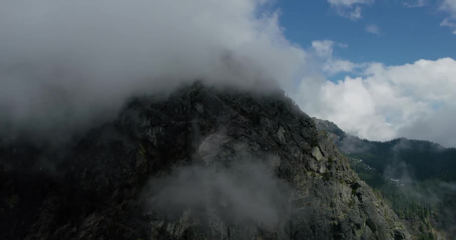 Aerial view pulling back from a rugged mountain peak partially hidden by swirling clouds