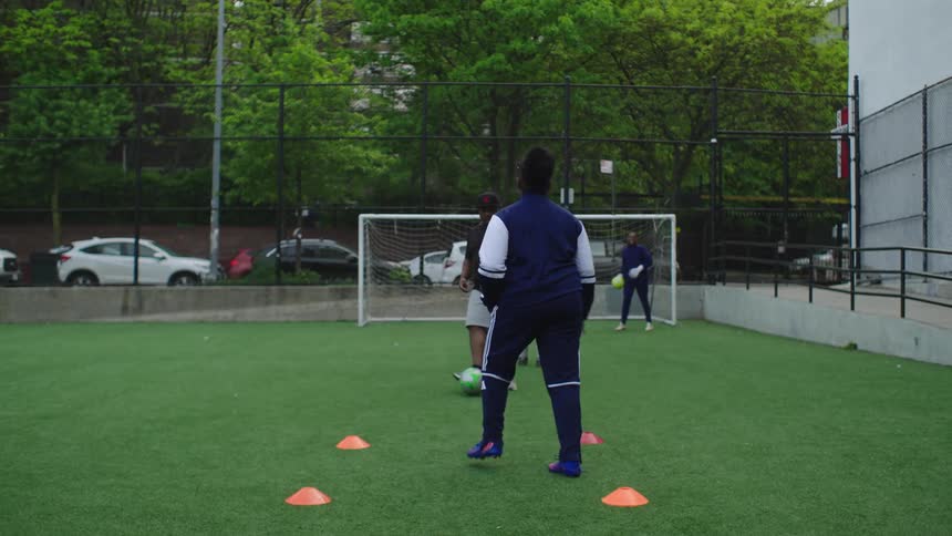 A young woman practices her soccer dribbling skills on an urban field under the guidance of her coach