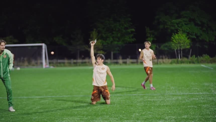 Soccer players engage in speed and agility drills during a night practice, with one player falling and then celebrating in slow motion