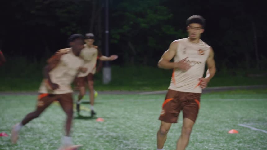 A diverse team of young male soccer players performs agility and speed drills on an illuminated field during a nighttime practice session